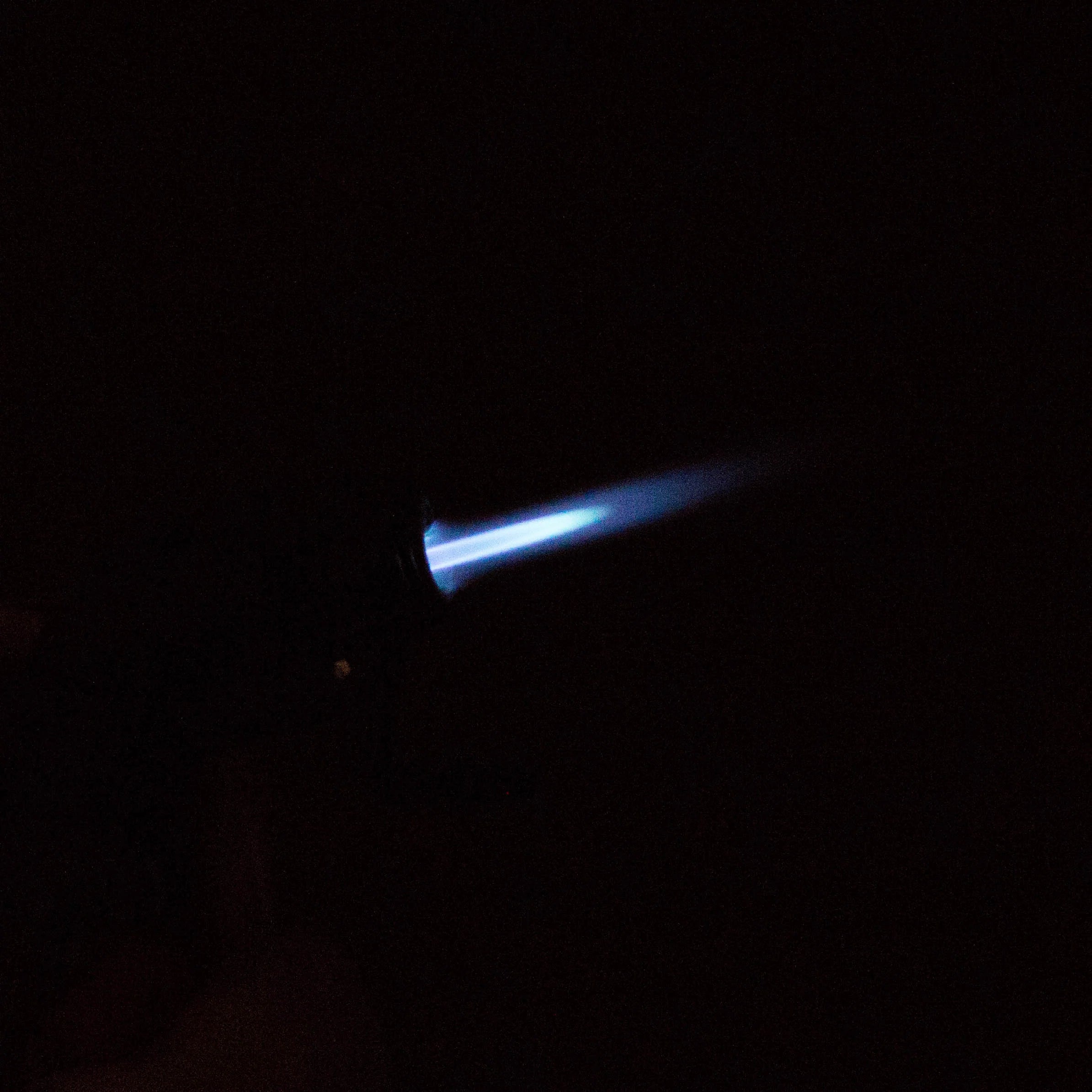 Eagle Torch PT116MOK mini torch lighter ignited, showing vivid blue jet flame against a black background – windproof flame in action.