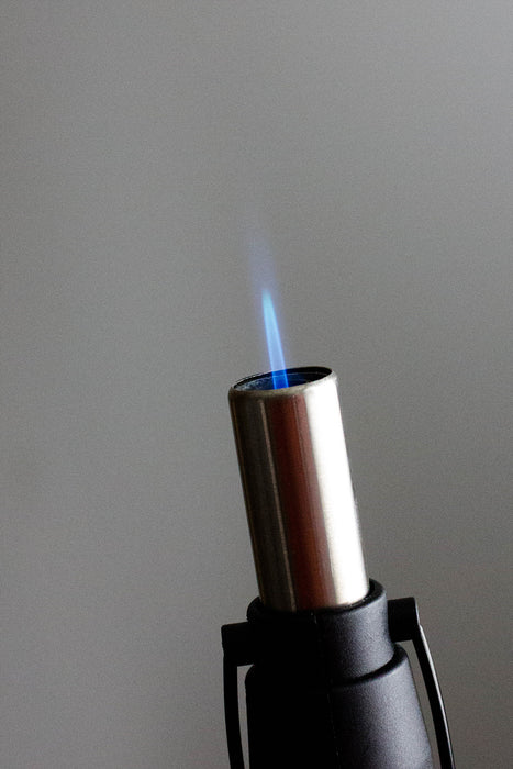 Close-up of a blue jet flame ignited from the extended nozzle of a red Eagle X-Pen refillable butane torch lighter, showcasing precise flame control.