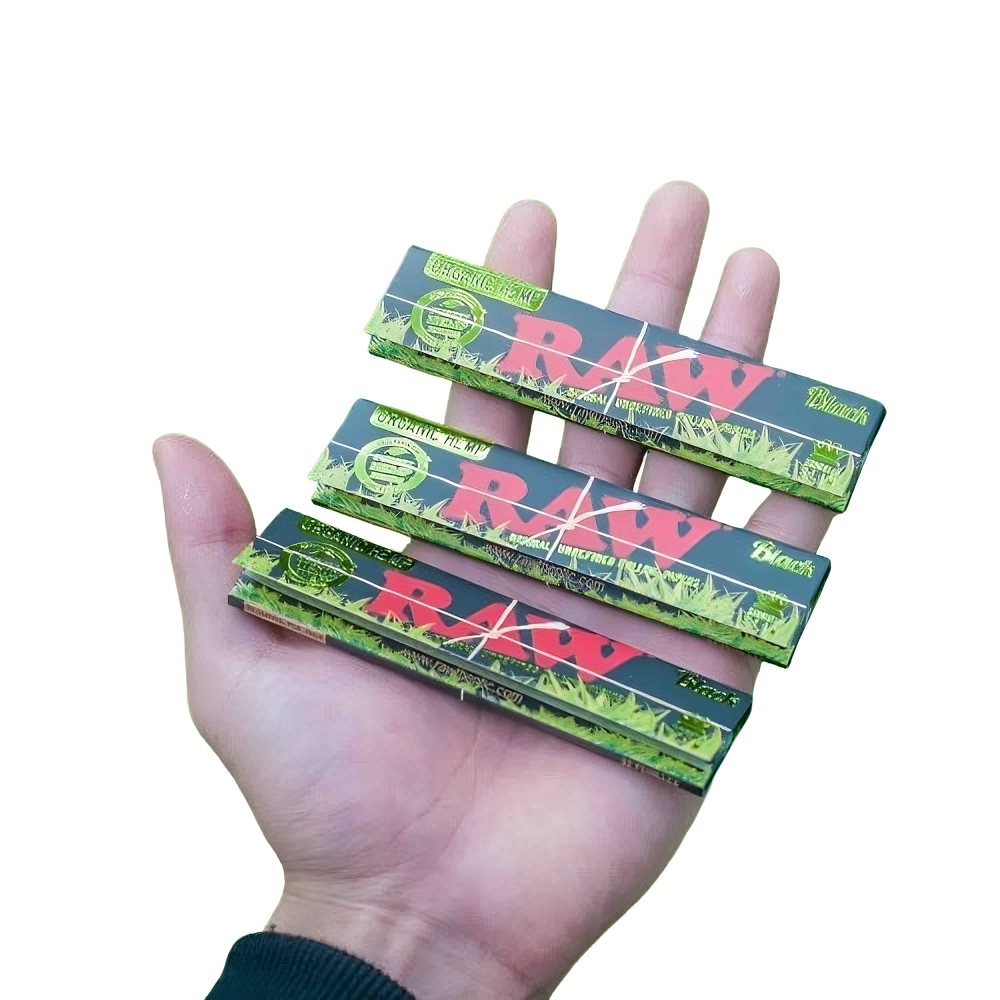 Hand holding three packs of RAW Black Organic Hemp King Size Slim Rolling Papers