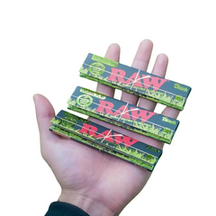 Hand holding three packs of RAW Black Organic Hemp King Size Slim Rolling Papers